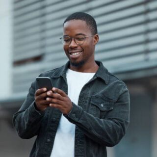 Black man, phone and social media in city reading text message or communication on social network app. African American person, chat conversation and happy on 5g mobile smartphone in Atlanta smile